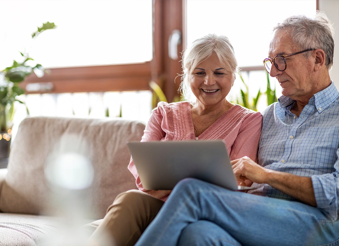 Service Center - A Senior Couple Looking at Their Laptop While Smiling on Their Living Room Couch